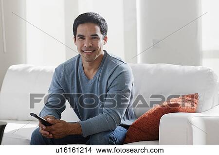 Picture - Portrait of smiling mid adult man sitting on sofa. Fotosearch