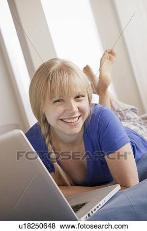 Portrait of smiling young woman lying on bed and using laptop View Large Photo Image Stock Photo - Portrait of smiling young woman lying on bed and using laptop. Fotosearch