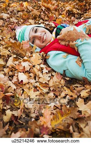 Portrait of smiling young woman lying on autumn leaves View Large Photo Image Stock Photograph - Portrait of smiling young woman lying on autumn leaves . Fotosearch