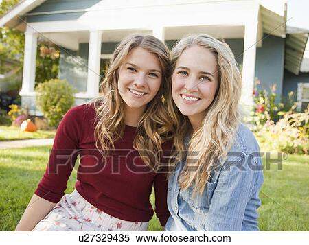 Stock Photography - Portrait of two young women cheek to cheek in front of house. Fotosearch