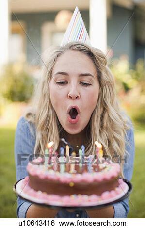 Stock Photograph - Portrait of young woman blowing birthday candles. Fotosearch