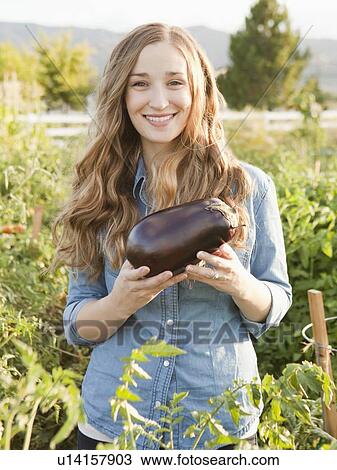 Stock Image - Portrait of young woman holding eggplant. Fotosearch