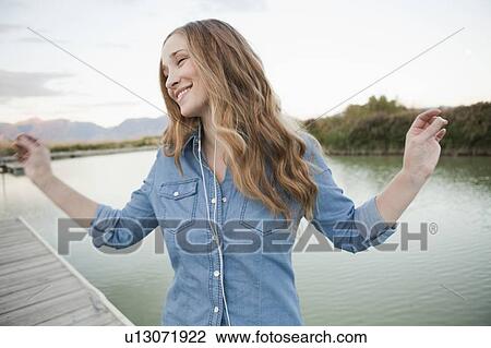 Portrait of young woman listening to mp3 player on jetty View Large Photo Image Stock Image - Portrait of young woman listening to mp3 player on jetty. Fotosearch