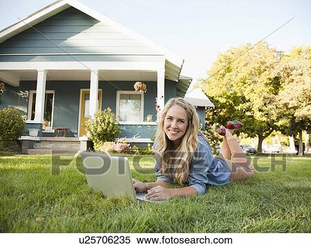 Stock Photography - Portrait of young woman lying down on grass with her laptop. Fotosearch