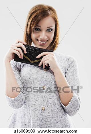 Stock Photo - Portrait of young woman showing purse, studio shot. Fotosearch