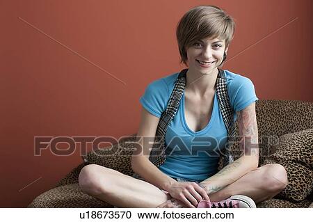 Stock Image - Portrait of young woman sitting on sofa. Fotosearch