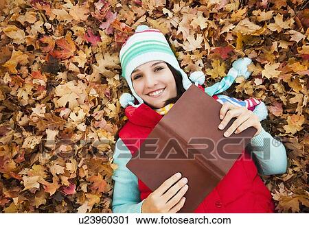 Portrait of young woman with book lying on autumn leaves View Large Photo Image Stock Image - Portrait of young woman with book lying on autumn leaves . Fotosearch