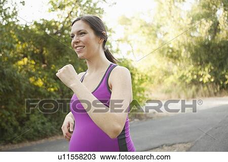 Stock Image - Pregnant mid adult woman in sport clothing jogging. Fotosearch