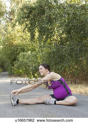 Stock Image - Pregnant mid adult woman in sport clothing stretching legs. Fotosearch