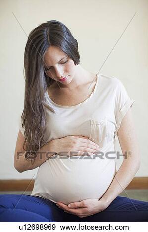 Pregnant mid adult woman looking down and touching her abdomen View Large Photo Image Stock Photo - Pregnant mid adult woman looking down and touching her abdomen. Fotosearch