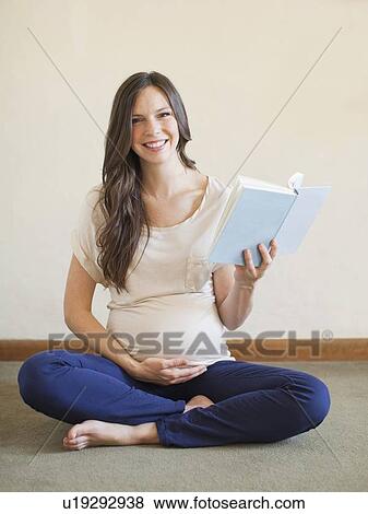 Pregnant mid adult woman sitting with crossed legs and holding book View Large Photo Image Stock Photo - Pregnant mid adult woman sitting with crossed legs and holding book. Fotosearch