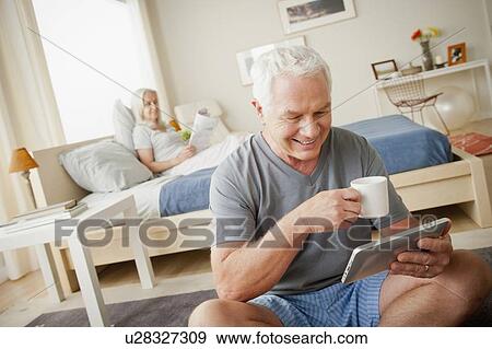 Senior man holding mug, woman sitting on bed in background View Large Photo Image Stock Photo - Senior man holding mug, woman sitting on bed in background. Fotosearch