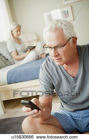 Senior man using mobile phone and senior woman reading book on bed View Large Photo Image Stock Photograph - Senior man using mobile phone and senior woman reading book on bed. Fotosearch