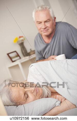 Stock Photograph - Senior man with coffee cup looking at sleeping wife. Fotosearch