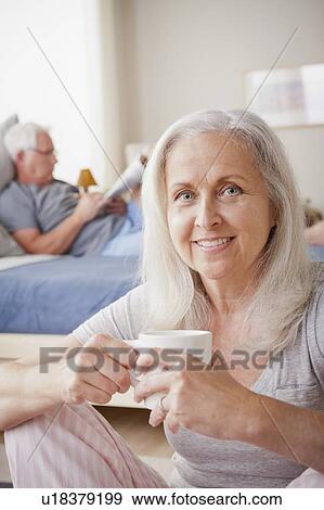 Senior woman holding mug, man sitting on bed in background View Large Photo Image Stock Photo - Senior woman holding mug, man sitting on bed in background. Fotosearch