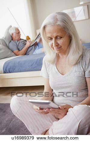 Stock Photo - Senior woman holding photo frame, man sitting on bed in background. Fotosearch