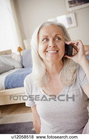 Stock Photo - Senior woman talking on phone with husband lying on bed. Fotosearch