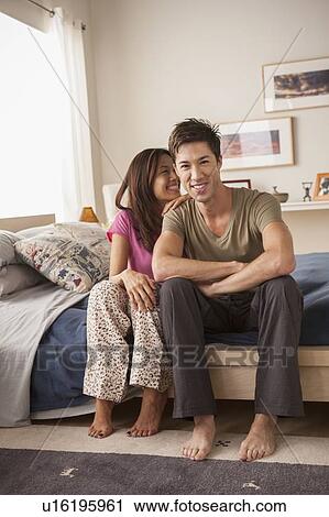 Smiling couple sitting on bed View Large Photo Image Stock Image - Smiling couple sitting on bed. Fotosearch