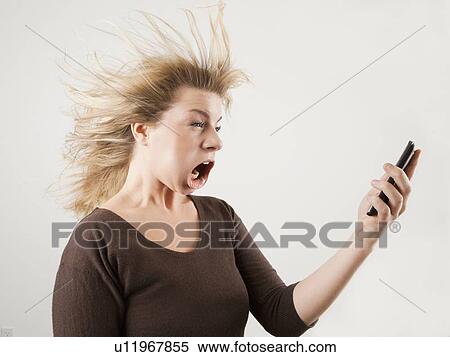Stock Photography - Studio shot of woman with windblown mouth holding phone. Fotosearch