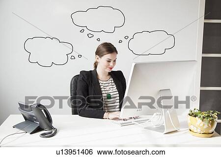 Stock Photograph - Studio shot of young woman working at desk with thought bubbles around her head. Fotosearch