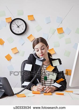 Picture - Studio shot of young woman working in office covered with adhesive notes. Fotosearch