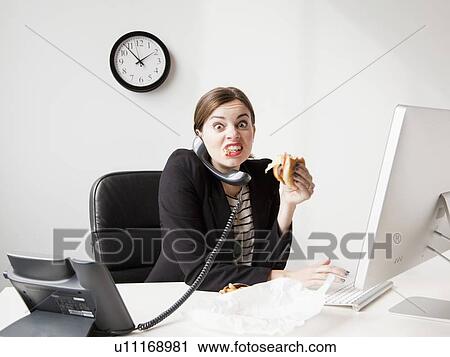 Studio shot of young woman working in office and having lunch same time View Large Photo Image Stock Image - Studio shot of young woman working in office and having lunch same time. Fotosearch