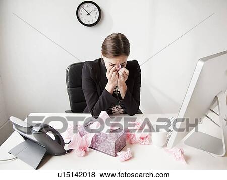 Stock Photo - Studio shot of young woman working in office sneezing. Fotosearch