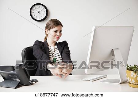 Stock Photo - Studio shot of young woman working in office and stretching her arms. Fotosearch