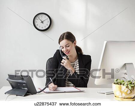 Stock Photo - Studio shot of young woman working in office talking on phone . Fotosearch