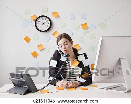Stock Photography - Studio shot of young woman working in office covered with adhesive notes. Fotosearch