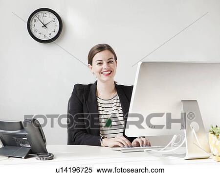 Stock Photography - Studio shot portrait of young woman working on computer and smiling. Fotosearch