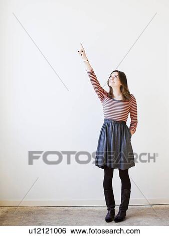 Stock Photograph - Studio shot young woman looking up and pointing. Fotosearch