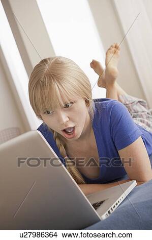 Surprised young woman lying on bed using laptop View Large Photo Image Picture - Surprised young woman lying on bed using laptop. Fotosearch
