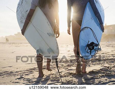 Stock Photo - Two female surfers walking on beach. Fotosearch