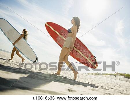 Two women carrying surfboards on beach View Large Photo Image Stock Image - Two women carrying surfboards on beach. Fotosearch