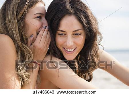 Stock Image - Two women whispering on beach. Fotosearch