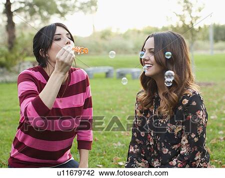 Two young women blowing bubbles in park View Large Photo Image Stock Image - Two young women blowing bubbles in park. Fotosearch