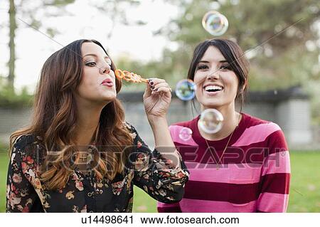 Two young women blowing bubbles in park View Large Photo Image Stock Image - Two young women blowing bubbles in park. Fotosearch