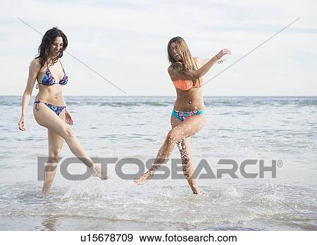 Stock Photo - Two young women splashing water on beach. Fotosearch