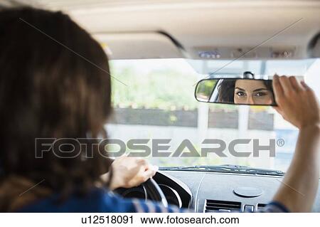 Stock Image - Woman adjusting rear view mirror in car. Fotosearch