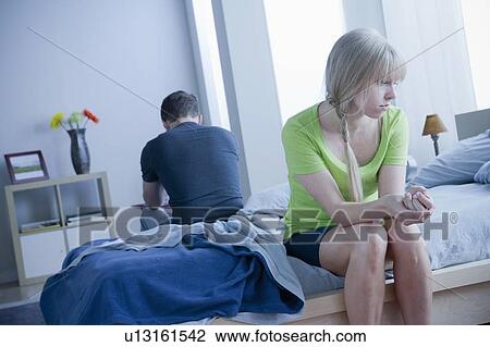 Stock Image - Woman and man sitting on bed back to back. Fotosearch