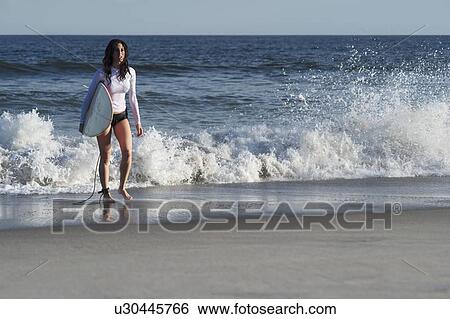 Stock Photograph - Woman carrying surfboard on beach. Fotosearch