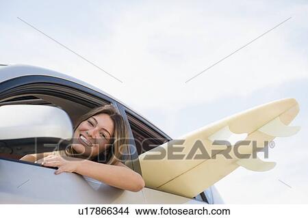 Picture - Woman driving car with surfboard inside. Fotosearch