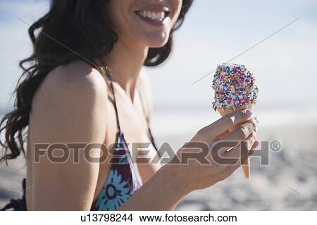 Picture - Woman eating icecream on beach. Fotosearch