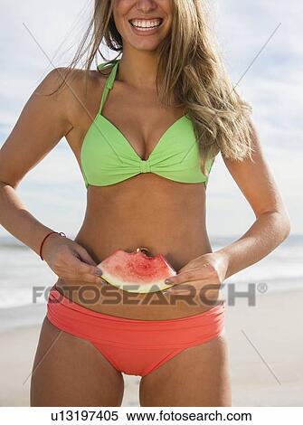 Stock Photography - Woman eating watermelon at beach. Fotosearch