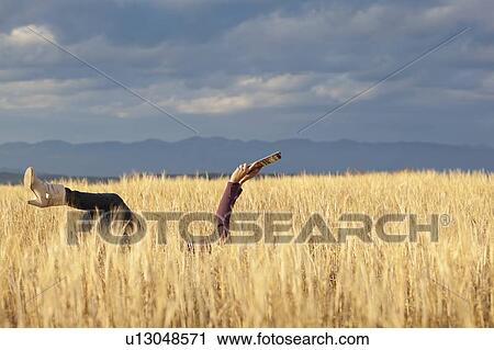 Stock Image - Woman lying in field holding digital tablet. Fotosearch