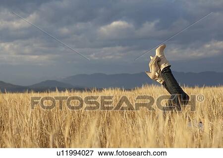 Stock Photo - Woman lying in scenic field with feet in air. Fotosearch