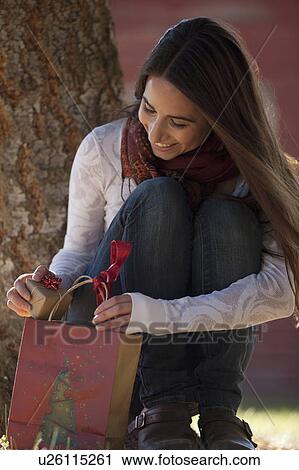 Stock Image - Woman opening gift bag and finding small wrapped gift. Fotosearch