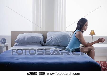 Woman sitting on bed in empty bedroom View Large Photo Image Stock Photo - Woman sitting on bed in empty bedroom. Fotosearch