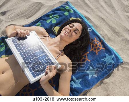 Stock Photo -  Woman sunbathing with solar panel at beach. Fotosearch